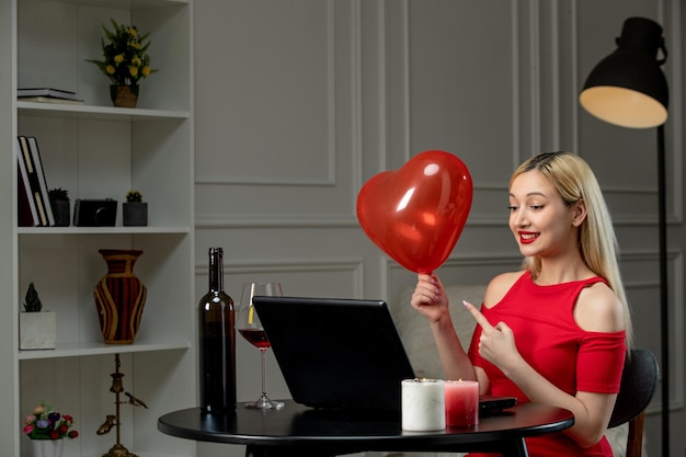 Amor virtual linda garota loira de vestido vermelho na data à distância com vinho segurando balão vermelho