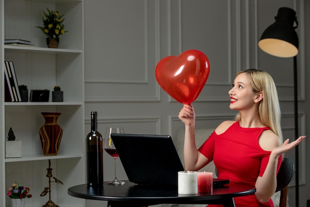 Amor virtual linda garota loira de vestido vermelho no encontro à distância com vinho olhando para o balão de coração