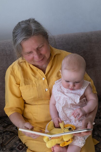 Amorosa abuela leyendo un libro a una niña sosteniendo un libro sentado en el sofá
