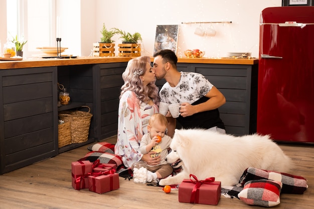Amorosa familia feliz con perro samoyedo disfrutando de su tiempo juntos en casa en la cocina en Navidad
