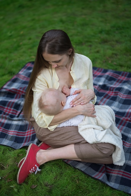 Amorosa madre abrazando a su bebé y amamanta. Picnic en el parque con recién nacido.