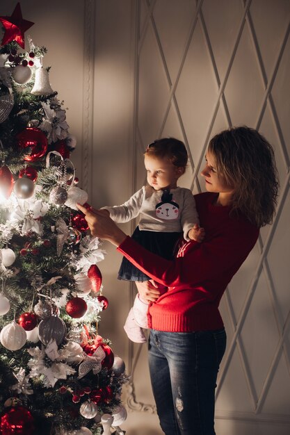 Amorosa madre con niña en manos de árbol de Navidad.