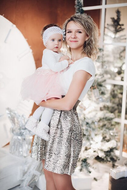 Amorosa madre con niña en manos de árbol de Navidad.