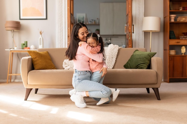 Amorosa mamá asiática abrazando a una adorable hijita en casa