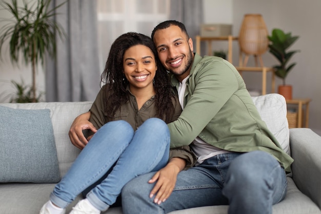 Amorosa pareja afroamericana abrazando posando sentada en casa