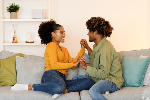 Amorosa pareja afroamericana tomados de la mano sentados en el sofá interior