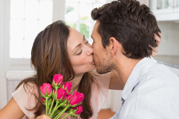 Amorosa pareja besándose con flores en la mano en casa