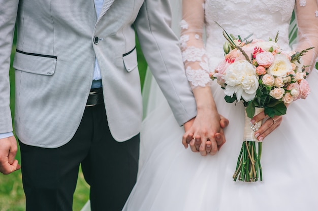 Amorosa pareja cogidos de la mano con anillos contra el vestido de novia