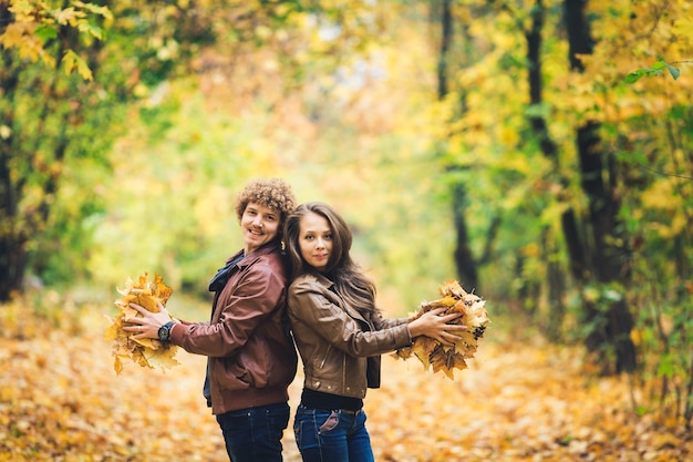 Amorosa pareja feliz en otoño en el parque con hojas de arce otoñal en las manos