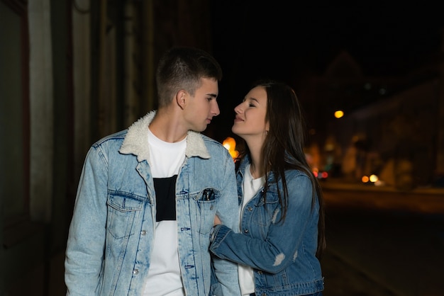 Amorosa pareja joven caminando por la calle. Pareja joven en una cita romántica por la noche. Ciudad de noche en el fondo.