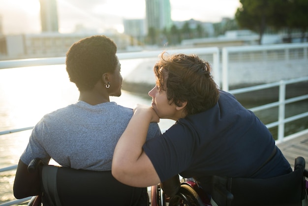 Amorosa pareja multicultural pasando el día juntos. Hombre afroamericano y mujer caucásica en sillas de ruedas, mirando la puesta de sol, apoyándose en el hombro. Amor, afecto, concepto de felicidad.