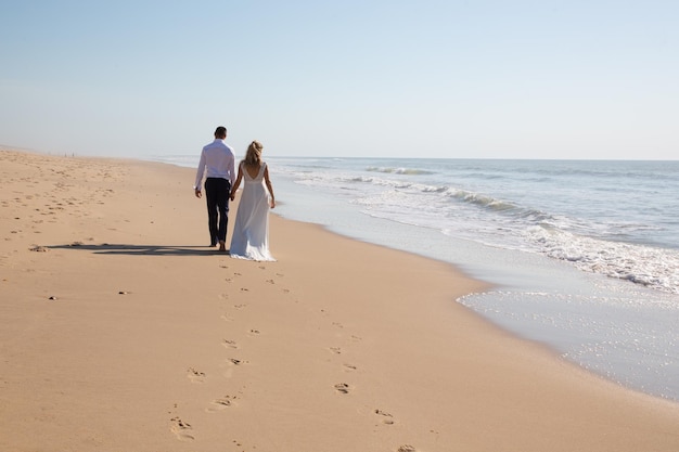 Amorosa pareja de novios caminando en la romántica playa de arena