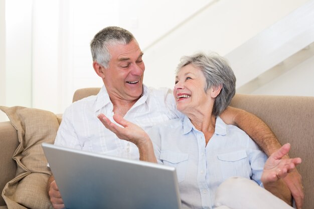 Amorosa pareja senior con portátil en el sofá