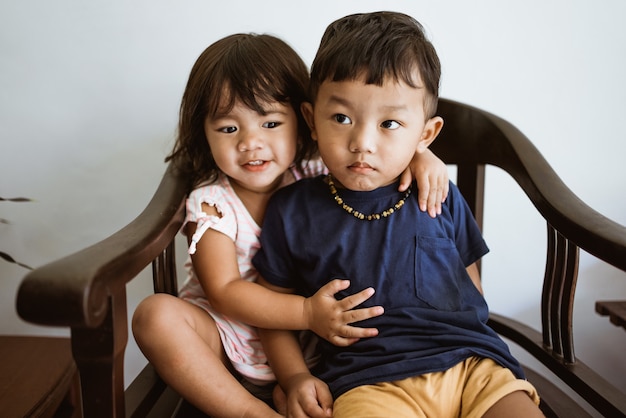 Amoroso hermano y hermana pequeña abrazándose mientras está sentado en una silla