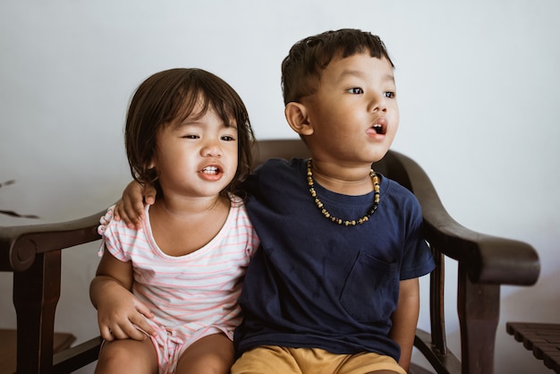 Amoroso hermano y hermana pequeña abrazándose mientras está sentado en una silla