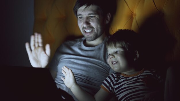 Amoroso padre y su pequeño hijo teniendo video chat en línea con los abuelos