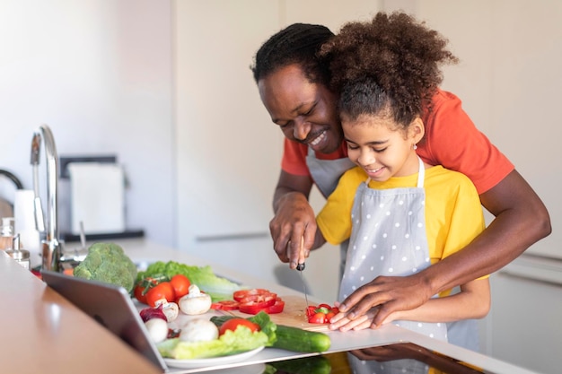 Amoroso pai negro ensinando sua filha a cozinhar comida na cozinha