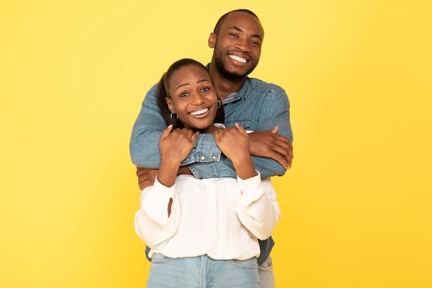 Amorosos cónyuges afroamericanos abrazándose posando sobre fondo amarillo de estudio