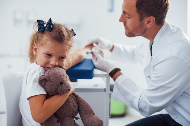 Amostra de sangue. Menina com seu ursinho de pelúcia está na clínica com o médico.