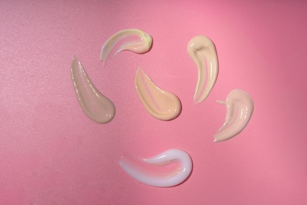 Amostras de base corretiva em creme, manchas variadas de diferentes tons, em um fundo rosa brilhante moderno