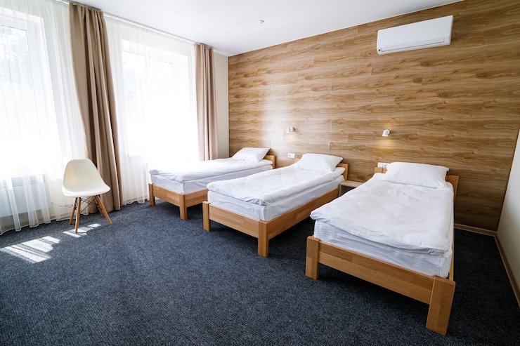 Foto amplia habitación luminosa en un albergue de tres camas. ropa de cama blanca