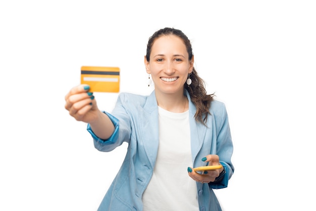 Amplia mujer sonriente está mostrando a la cámara su tarjeta de crédito y su teléfono.