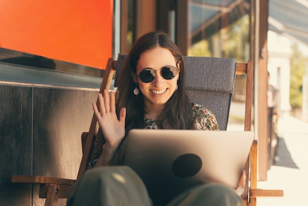 Amplia mujer sonriente está saludando a la persona que está hablando en su computadora portátil.