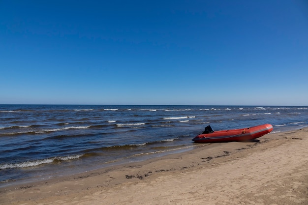 Amplia playa de arena vacía con bote de goma de estacionamiento en el borde del agua y la tierra sobre un fondo de cielo azul claro, lugar para el texto.