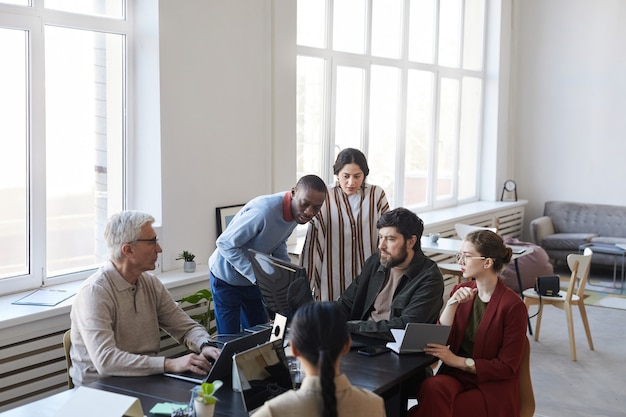 Foto amplio ángulo de visión en diverso grupo de gente de negocios reunida en la oficina y usando la computadora mientras se discute el proyecto, copie el espacio