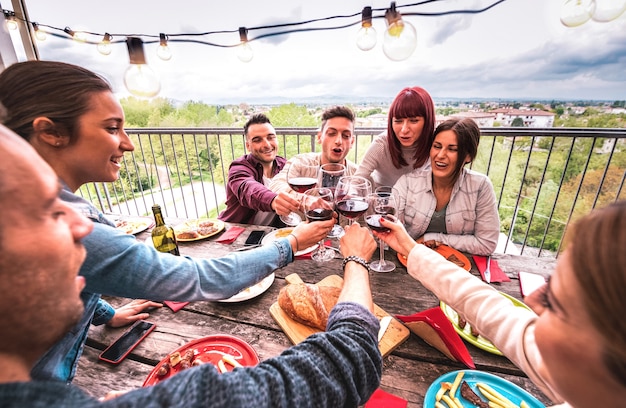 Amplio ángulo de visión de gente feliz brindando vino tinto juntos en la fiesta de la azotea en una villa al aire libre