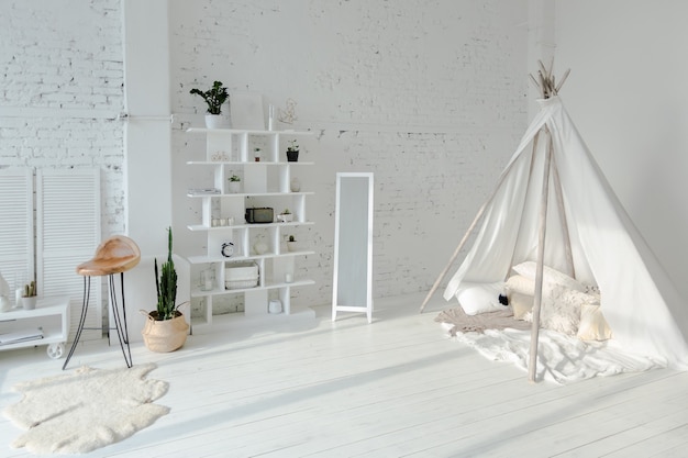 Amplio y elegante apartamento tipo loft moderno en colores blanco y gris lleno de luz solar. pared de ladrillo y casa de niños en forma de tipi.