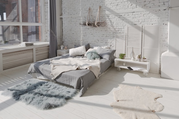 Amplio y elegante apartamento tipo loft moderno en colores blanco y gris lleno de luz solar. pared de ladrillo, estantería, cama de plataforma