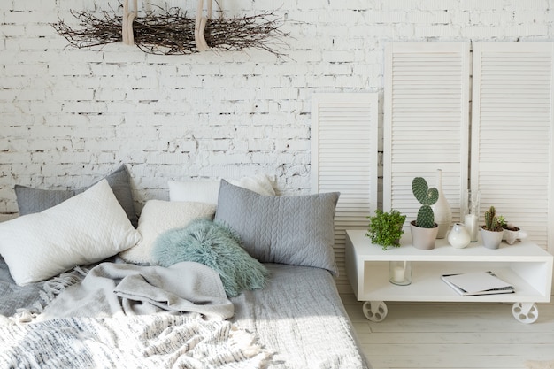 Amplio y elegante apartamento tipo loft moderno en colores blanco y gris lleno de luz solar. pared de ladrillos, estanterías, cama tipo paleta y casita infantil en forma de tipi.