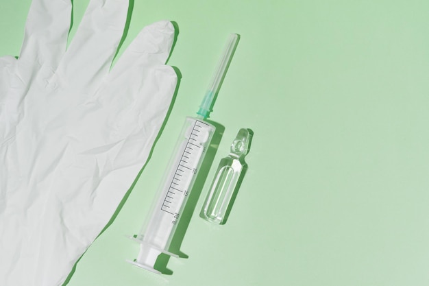 Ampola transparente farmacêutica com seringa de medicação e luva de borracha branca sobre fundo verde isolado Terapia de beleza e vacinação contra o conceito de doenças Lugar para o seu projeto
