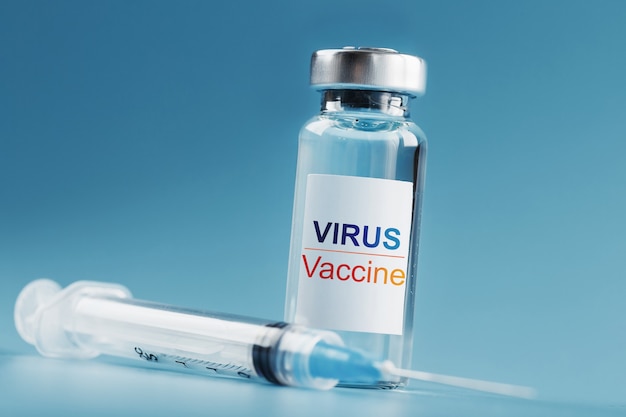Ampolla y jeringa con la vacuna contra el Virus contra enfermedades sobre un fondo azul.