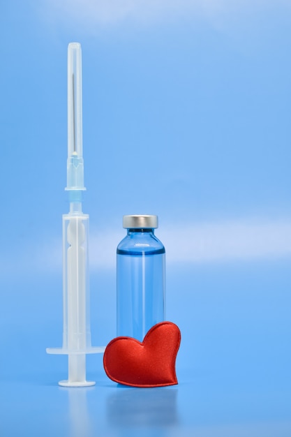 Ampollas de vidrio, corazón rojo y jeringa sobre fondo azul. medicina, vacunación, productos farmacéuticos