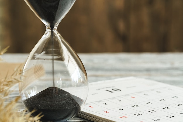 Foto ampulheta com calendário na mesa de madeira fechar