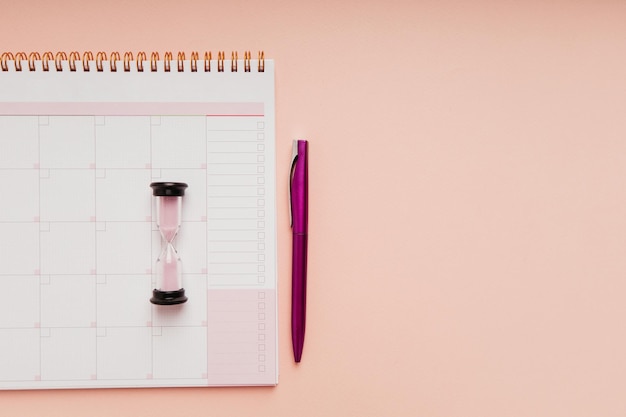 Ampulheta com planejador de mês e caneta em um conceito de gerenciamento de tempo de fundo rosa