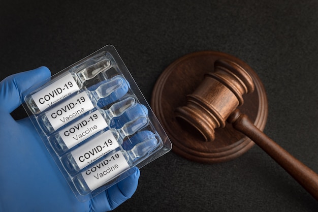 Ampullen mit Impfstoff gegen Coronavirus und Richterhammer. Gesetze und Entscheidungen gegen covid-19