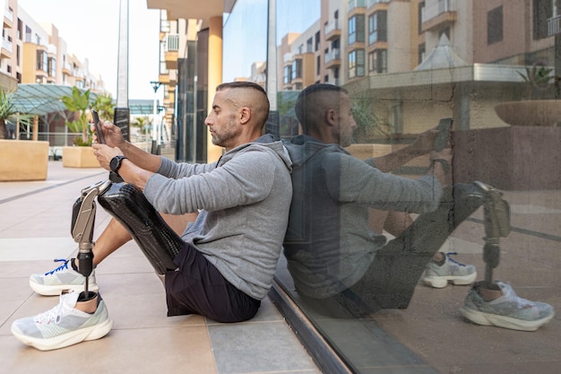 Amputado masculino usando smartphone perto da parede de vidro