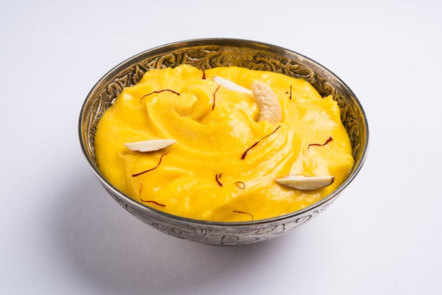 Amrakhand é um iogurte com sabor de Alphonso ou Shrikhand, popular doce indiano servido com frutas secas e açafrão com manga inteira, sobre fundo colorido. foco seletivo