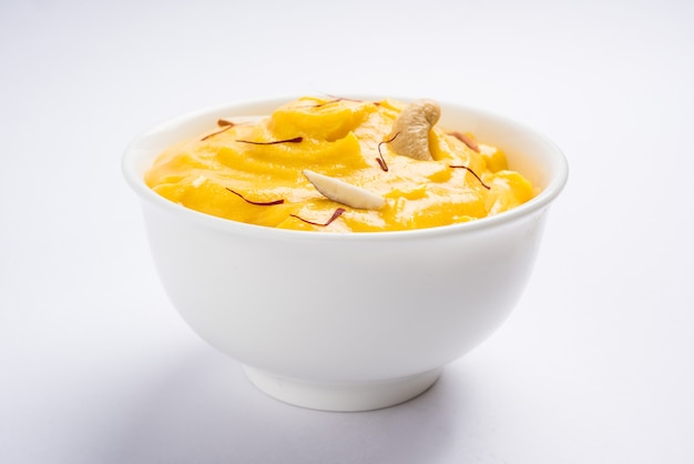 Amrakhand é um iogurte com sabor de Alphonso ou Shrikhand, popular doce indiano servido com frutas secas e açafrão com manga inteira, sobre fundo colorido. foco seletivo