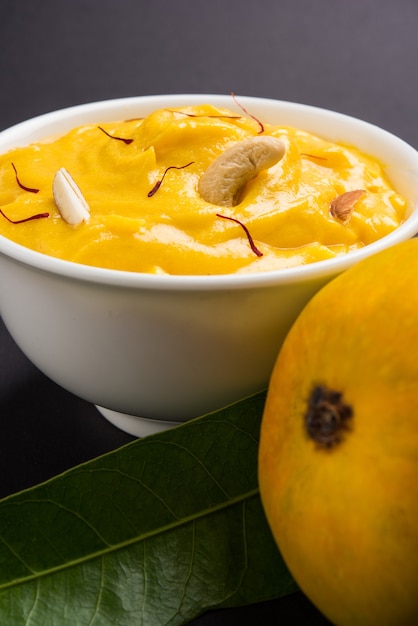 Amrakhand é um iogurte com sabor de Alphonso ou Shrikhand, popular doce indiano servido com frutas secas e açafrão com manga inteira, sobre fundo colorido. foco seletivo