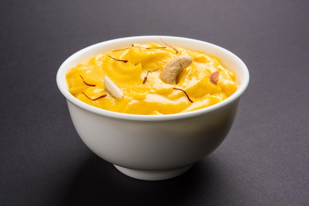 Amrakhand é um iogurte com sabor de Alphonso ou Shrikhand, popular doce indiano servido com frutas secas e açafrão com manga inteira, sobre fundo colorido. foco seletivo