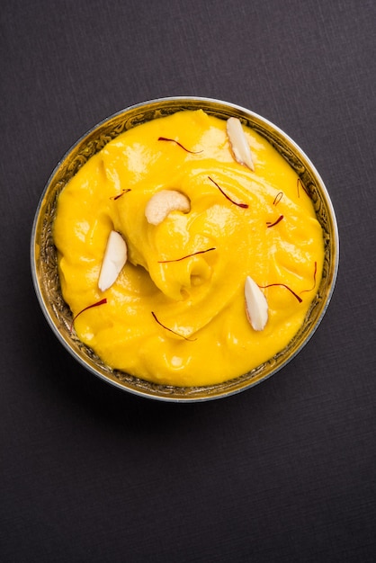 Amrakhand é um iogurte com sabor de Alphonso ou Shrikhand, popular doce indiano servido com frutas secas e açafrão com manga inteira, sobre fundo colorido. foco seletivo