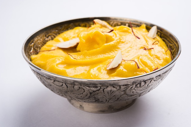 Amrakhand es un yogur con sabor a Alfonso o Shrikhand, dulce popular indio servido con frutas secas y azafrán con mango entero, sobre un fondo colorido. enfoque selectivo