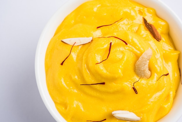 Amrakhand es un yogur con sabor a Alfonso o Shrikhand, dulce popular indio servido con frutas secas y azafrán con mango entero, sobre un fondo colorido. enfoque selectivo