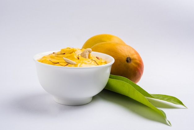 Amrakhand ist ein Joghurt mit Alphonso-Geschmack oder Shrikhand, eine beliebte indische Süßigkeit, die mit Trockenfrüchten und Safran mit ganzen Mangofrüchten auf buntem Hintergrund serviert wird. selektiver Fokus