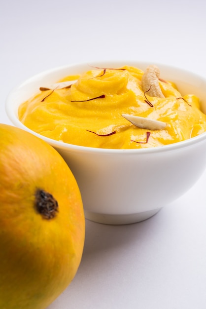 Amrakhand ist ein Joghurt mit Alphonso-Geschmack oder Shrikhand, eine beliebte indische Süßigkeit, die mit Trockenfrüchten und Safran mit ganzen Mangofrüchten auf buntem Hintergrund serviert wird. selektiver Fokus