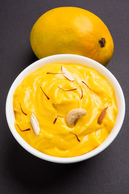 Amrakhand ist ein Joghurt mit Alphonso-Geschmack oder Shrikhand, eine beliebte indische Süßigkeit, die mit Trockenfrüchten und Safran mit ganzen Mangofrüchten auf buntem Hintergrund serviert wird. selektiver Fokus